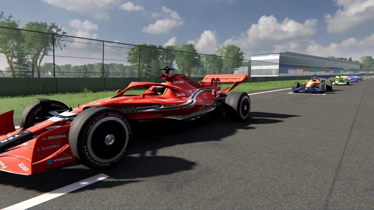 A red modern car on the starting grid, with the rest of the field ahead